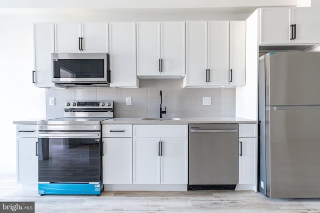 kitchen with appliances with stainless steel finishes, sink, light wood-type flooring, white cabinetry, and tasteful backsplash