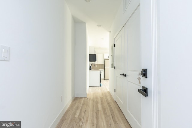 corridor with light wood-type flooring and sink