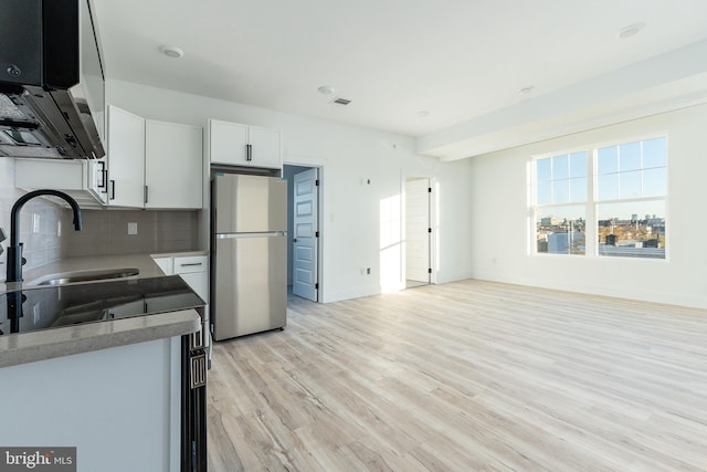 kitchen with light wood-type flooring, stainless steel fridge, sink, tasteful backsplash, and white cabinets