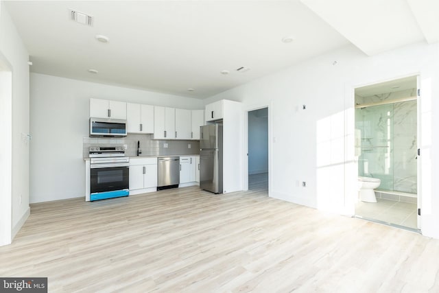 kitchen featuring appliances with stainless steel finishes, white cabinets, decorative backsplash, sink, and light wood-type flooring