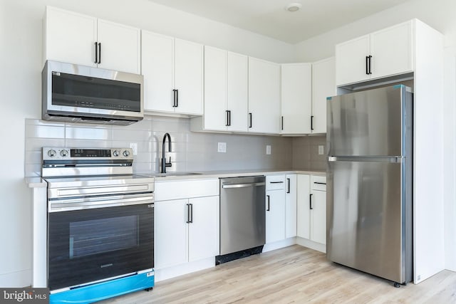 kitchen with light hardwood / wood-style flooring, sink, backsplash, appliances with stainless steel finishes, and white cabinets