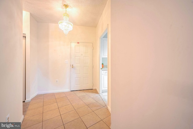 hallway featuring an inviting chandelier, a textured ceiling, and light tile patterned floors