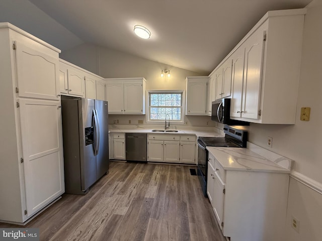 kitchen with lofted ceiling, appliances with stainless steel finishes, sink, and white cabinets