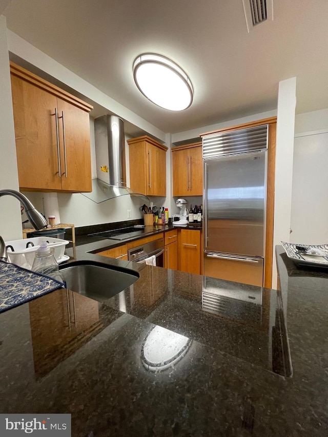 kitchen with cooktop, sink, stainless steel built in fridge, dark stone countertops, and extractor fan