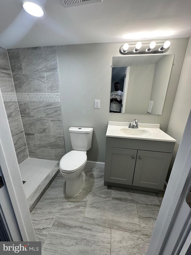 bathroom featuring vanity, a tile shower, and toilet