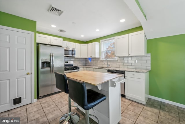 kitchen with stainless steel appliances, a kitchen bar, white cabinets, and sink