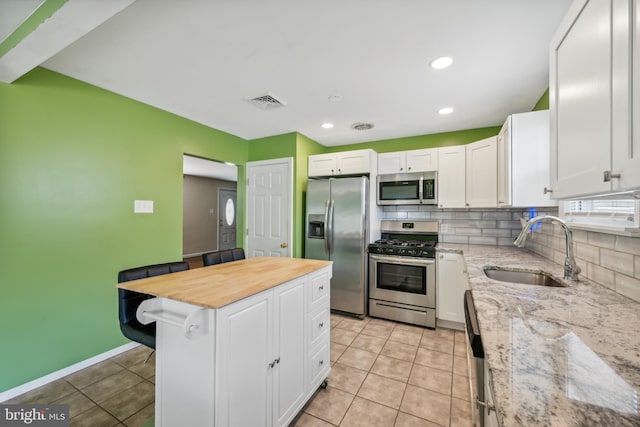 kitchen featuring sink, light stone counters, appliances with stainless steel finishes, a center island, and white cabinets