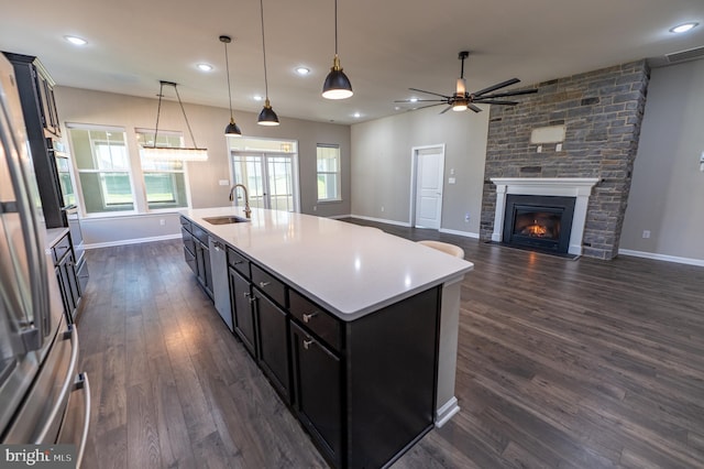 kitchen featuring a stone fireplace, a center island with sink, sink, and pendant lighting