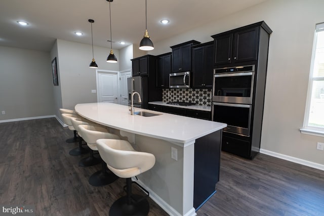 kitchen featuring a center island with sink, stainless steel appliances, hanging light fixtures, sink, and a kitchen breakfast bar