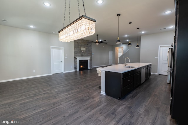 kitchen with dark hardwood / wood-style flooring, sink, a kitchen island with sink, a fireplace, and decorative light fixtures