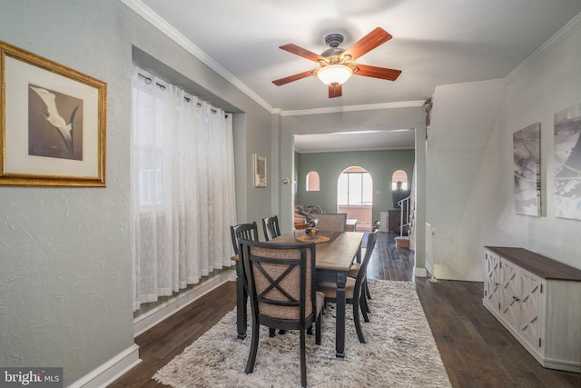 dining space featuring crown molding, a ceiling fan, arched walkways, baseboards, and dark wood-type flooring