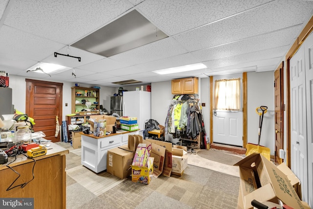 basement featuring a paneled ceiling, light colored carpet, and stainless steel refrigerator