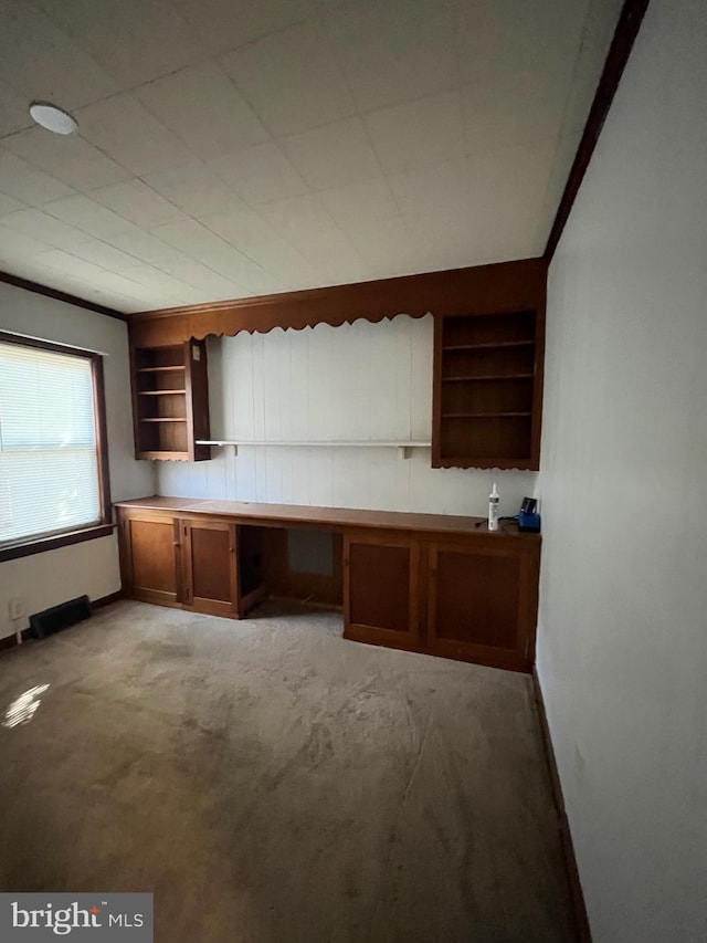 unfurnished office with ornamental molding, carpet floors, and built in shelves