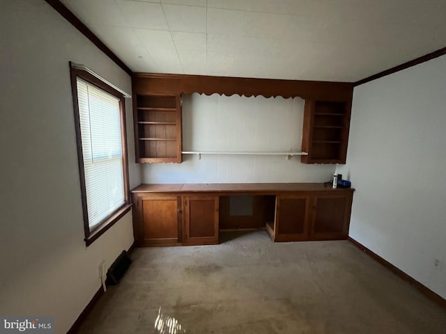 unfurnished office with built in desk, crown molding, light colored carpet, and built in features