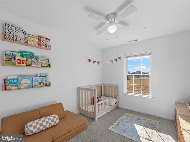 bedroom with a nursery area, light colored carpet, and ceiling fan