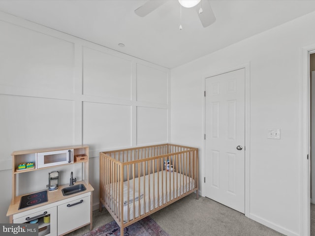 carpeted bedroom featuring a crib and ceiling fan