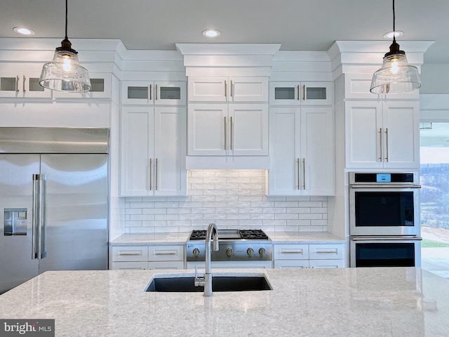 kitchen with light stone countertops, sink, hanging light fixtures, white cabinetry, and stainless steel appliances