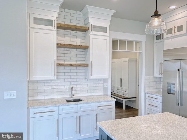 kitchen with high end refrigerator, sink, backsplash, decorative light fixtures, and white cabinets