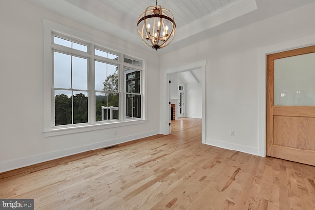 unfurnished dining area with a notable chandelier, a tray ceiling, light wood-type flooring, and crown molding