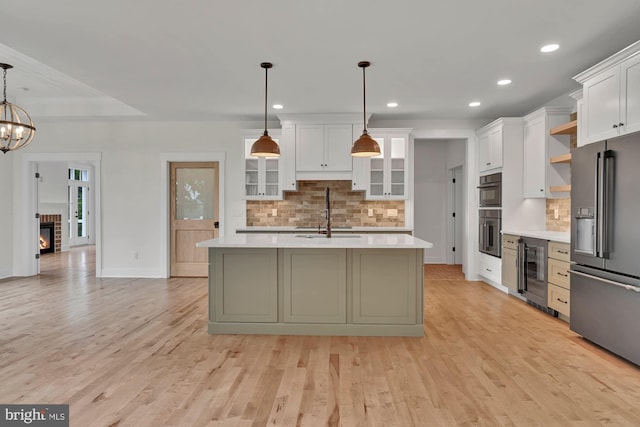 kitchen with hanging light fixtures, a center island with sink, sink, beverage cooler, and appliances with stainless steel finishes