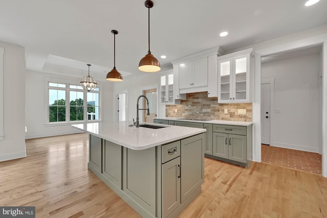 kitchen with black electric stovetop, an island with sink, hanging light fixtures, light hardwood / wood-style flooring, and sink