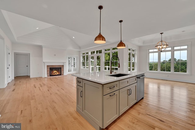 kitchen featuring an island with sink, light hardwood / wood-style flooring, gray cabinetry, sink, and stainless steel dishwasher