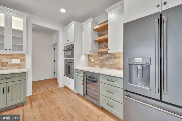 kitchen with appliances with stainless steel finishes, wine cooler, light hardwood / wood-style floors, and backsplash