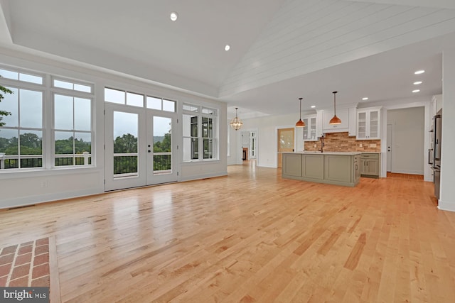 unfurnished living room featuring an inviting chandelier, light hardwood / wood-style flooring, and high vaulted ceiling