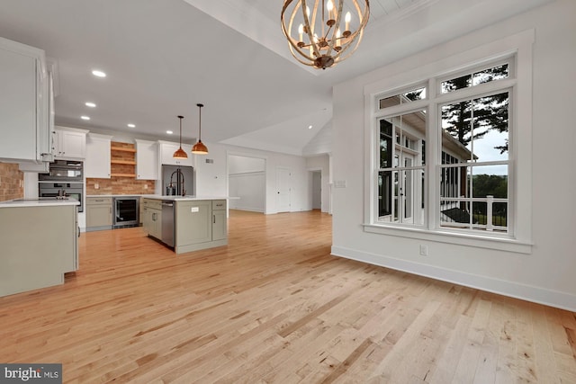 kitchen with beverage cooler, an island with sink, white cabinetry, light wood-type flooring, and decorative light fixtures