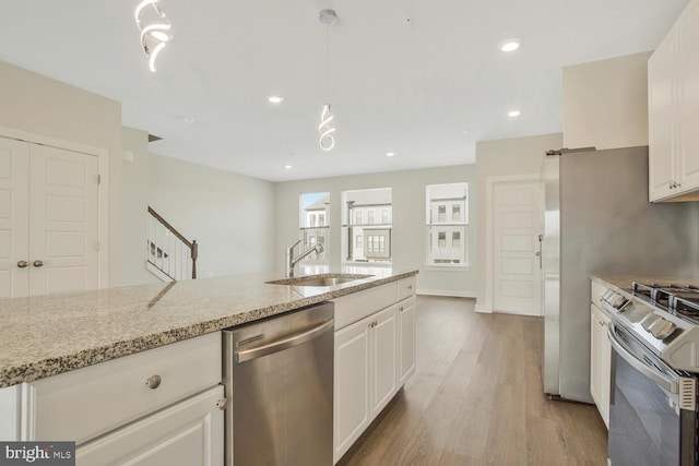 kitchen with appliances with stainless steel finishes, sink, hanging light fixtures, white cabinetry, and light hardwood / wood-style flooring