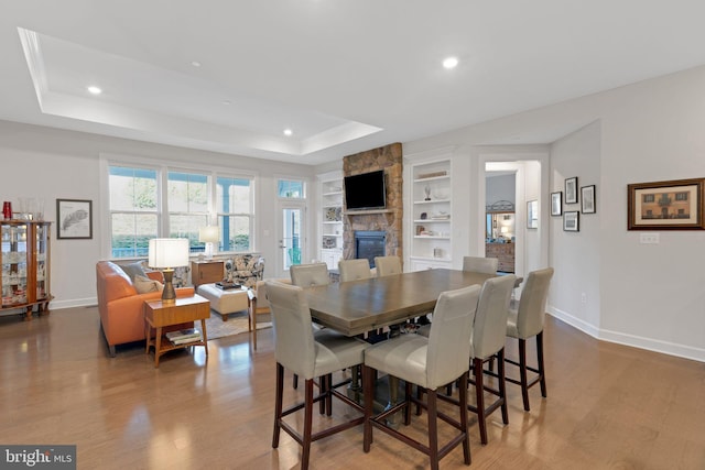 dining space with a tray ceiling, a fireplace, built in features, and light wood-type flooring