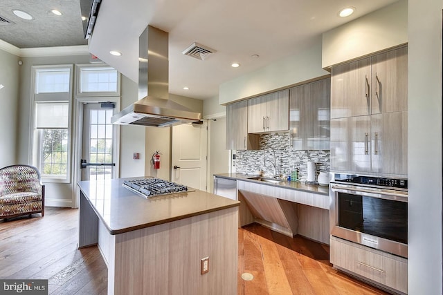 kitchen featuring appliances with stainless steel finishes, island range hood, sink, light hardwood / wood-style floors, and a kitchen island