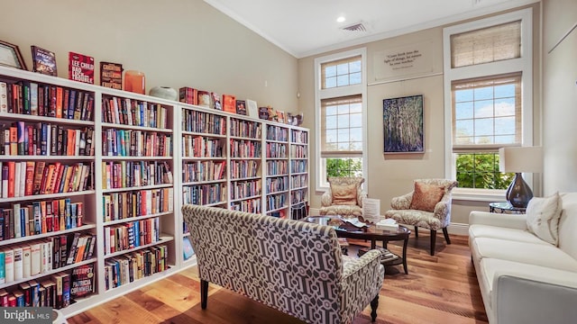 living area featuring a wealth of natural light, a towering ceiling, light hardwood / wood-style floors, and ornamental molding