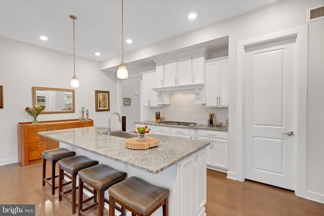 kitchen featuring a center island with sink, white cabinets, and decorative light fixtures