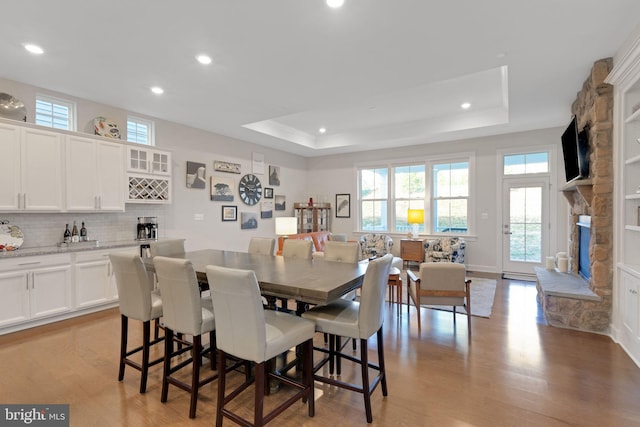 dining area with a fireplace, a tray ceiling, light hardwood / wood-style flooring, and a wealth of natural light