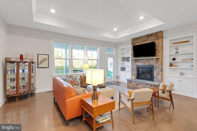 living room featuring a fireplace, built in shelves, light wood-type flooring, and a tray ceiling