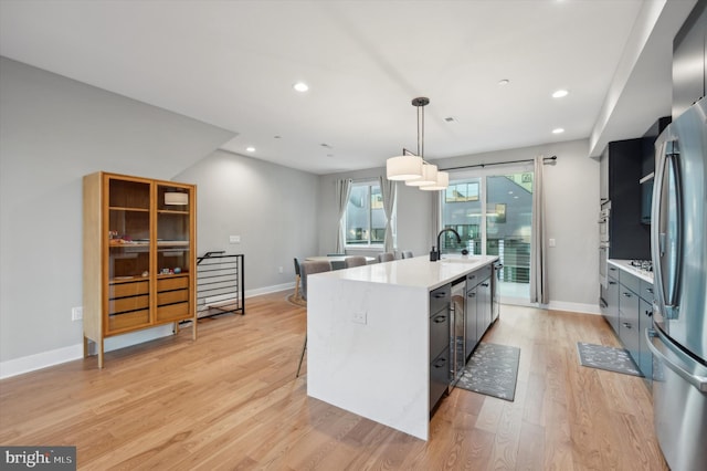 kitchen with stainless steel fridge, a kitchen island with sink, light hardwood / wood-style flooring, sink, and decorative light fixtures