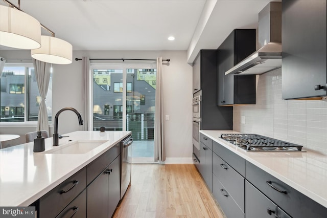 kitchen featuring wall chimney range hood, light hardwood / wood-style flooring, sink, plenty of natural light, and appliances with stainless steel finishes