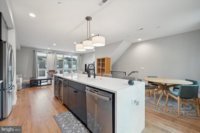 kitchen featuring sink, light hardwood / wood-style floors, stainless steel appliances, decorative light fixtures, and a kitchen island with sink