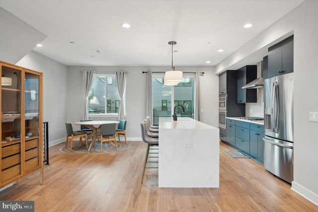 kitchen with hanging light fixtures, a breakfast bar area, an island with sink, light wood-type flooring, and stainless steel appliances