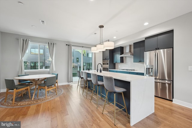 kitchen featuring wall chimney exhaust hood, a breakfast bar area, pendant lighting, appliances with stainless steel finishes, and light hardwood / wood-style floors