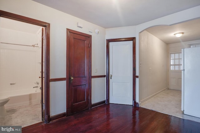 unfurnished bedroom with white fridge, ensuite bath, and wood-type flooring