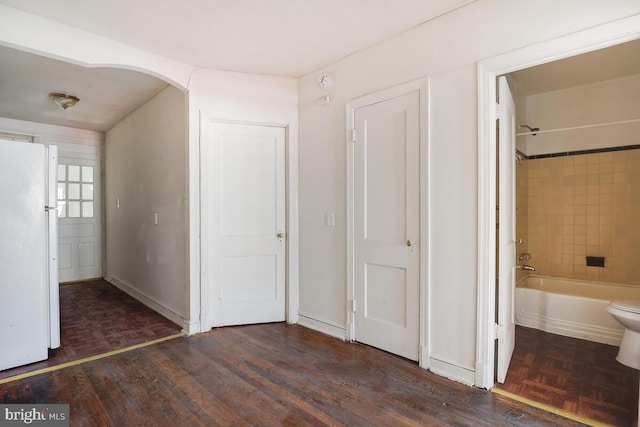 unfurnished bedroom with connected bathroom, white refrigerator, and dark hardwood / wood-style floors