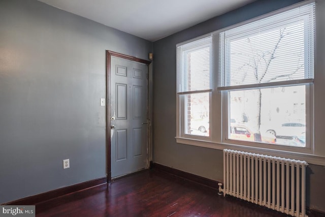 spare room featuring dark hardwood / wood-style floors, radiator, and plenty of natural light