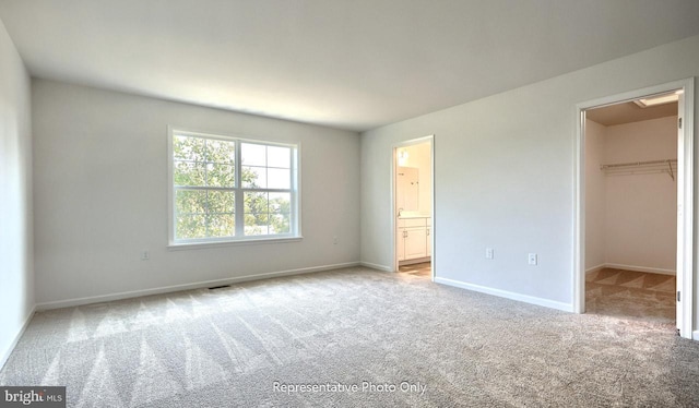 unfurnished bedroom with a closet, light colored carpet, a spacious closet, and ensuite bath