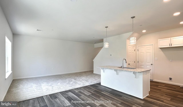 kitchen with sink, dark wood-type flooring, pendant lighting, a breakfast bar area, and white cabinets