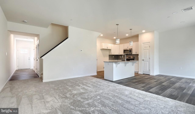 kitchen featuring backsplash, dark wood-type flooring, pendant lighting, a center island with sink, and white cabinetry