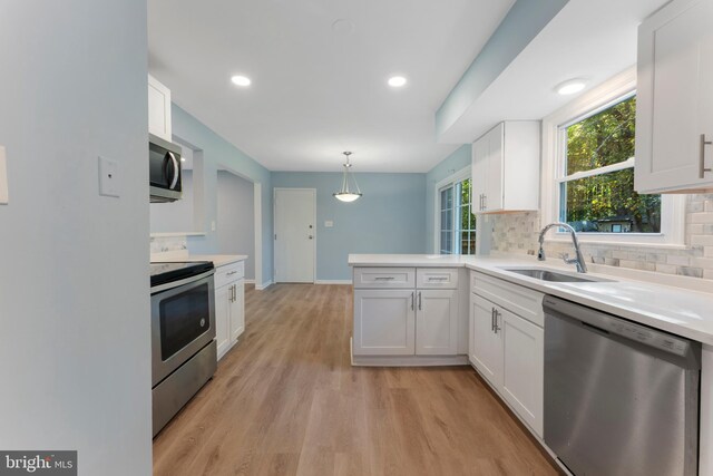 kitchen with appliances with stainless steel finishes, white cabinets, hanging light fixtures, and light hardwood / wood-style floors