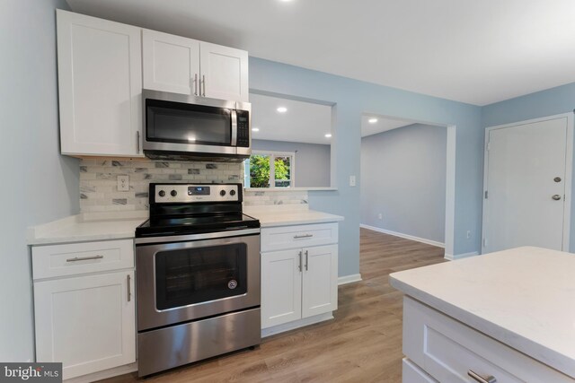 kitchen featuring white cabinetry, stainless steel appliances, light wood-type flooring, and backsplash