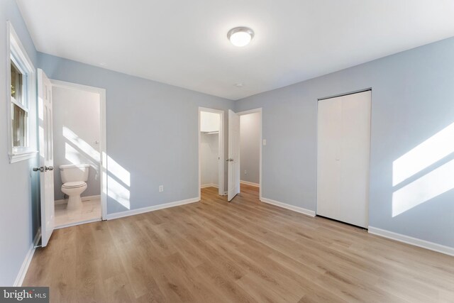 unfurnished bedroom with multiple windows, light wood-type flooring, and ensuite bath